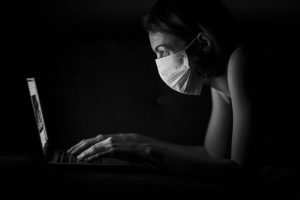 A woman wearing a facemask using a laptop in a dark room