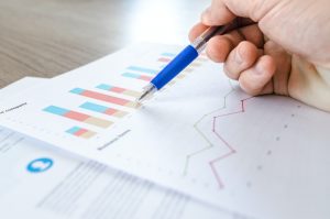 a hand using a pen to point at a bar chart on a printed piece of paper.