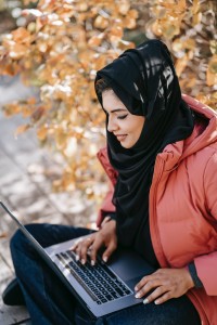 a woman sat outside in autumn, wearing a coat as she types on a laptop