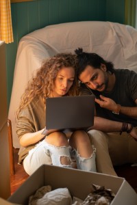 A man and woman sat together on a sofa in a cosy setting, looking at a laptop together