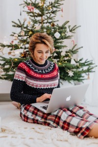A woman sat on a rug with a laptop on her knee as if working, with a Christmas tree behind her.