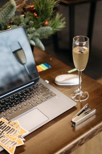 a glass of champagne sat on a desk next to an open laptop, decorations reading 'happy new year' strewn over the keyboard.