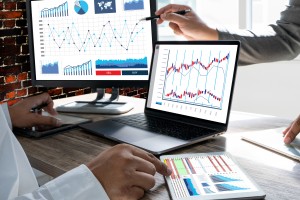 2 computer screens on a desk displaying various analytics readouts and graphs